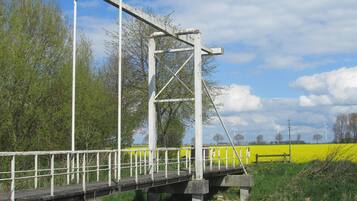Een metalen brug met een houten looppad, omgeven door groen en velden.