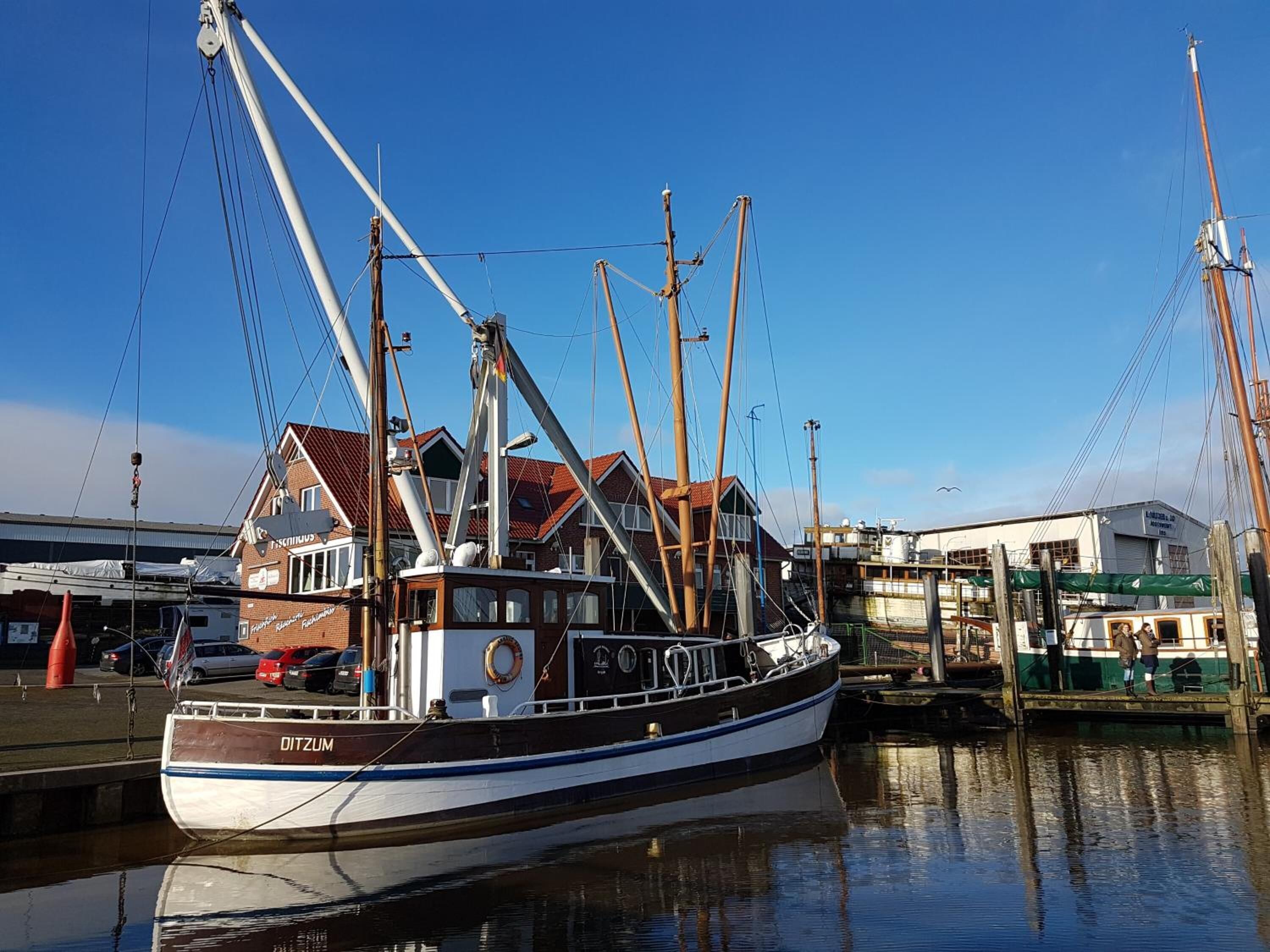Ein Boot liegt in einer Marina vor einem Gebäude im Hintergrund.