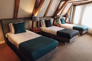 Une chambre avec trois lits, des poutres en bois au plafond et un sol recouvert de moquette.