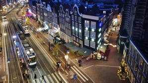 A tram moving along a street lined with historic buildings, some with illuminated signs. - Hotel Corner House (Amsterdam)