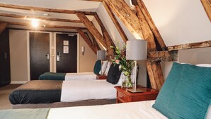 A room with two beds, wooden beams, a nightstand with a lamp, and a door. - Hotel Corner House (Amsterdam)