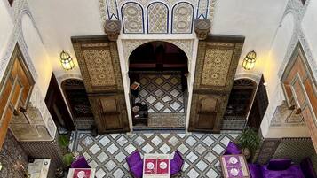 An ornate courtyard with intricate tile work, a central archway, and seating areas with purple cushions.
