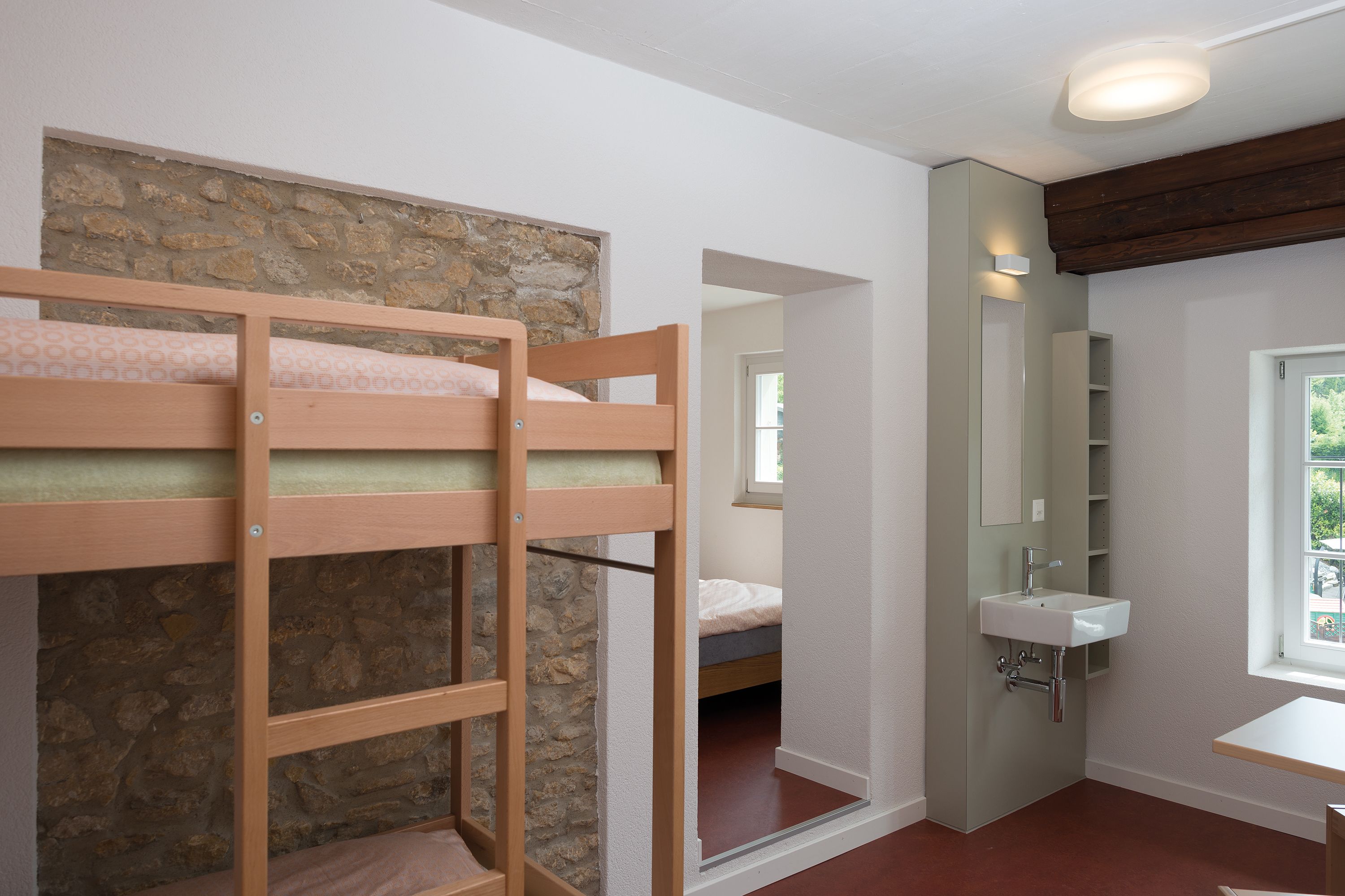 A bedroom with bunk beds, a stone wall, a bathroom with a sink and mirror, and a window.