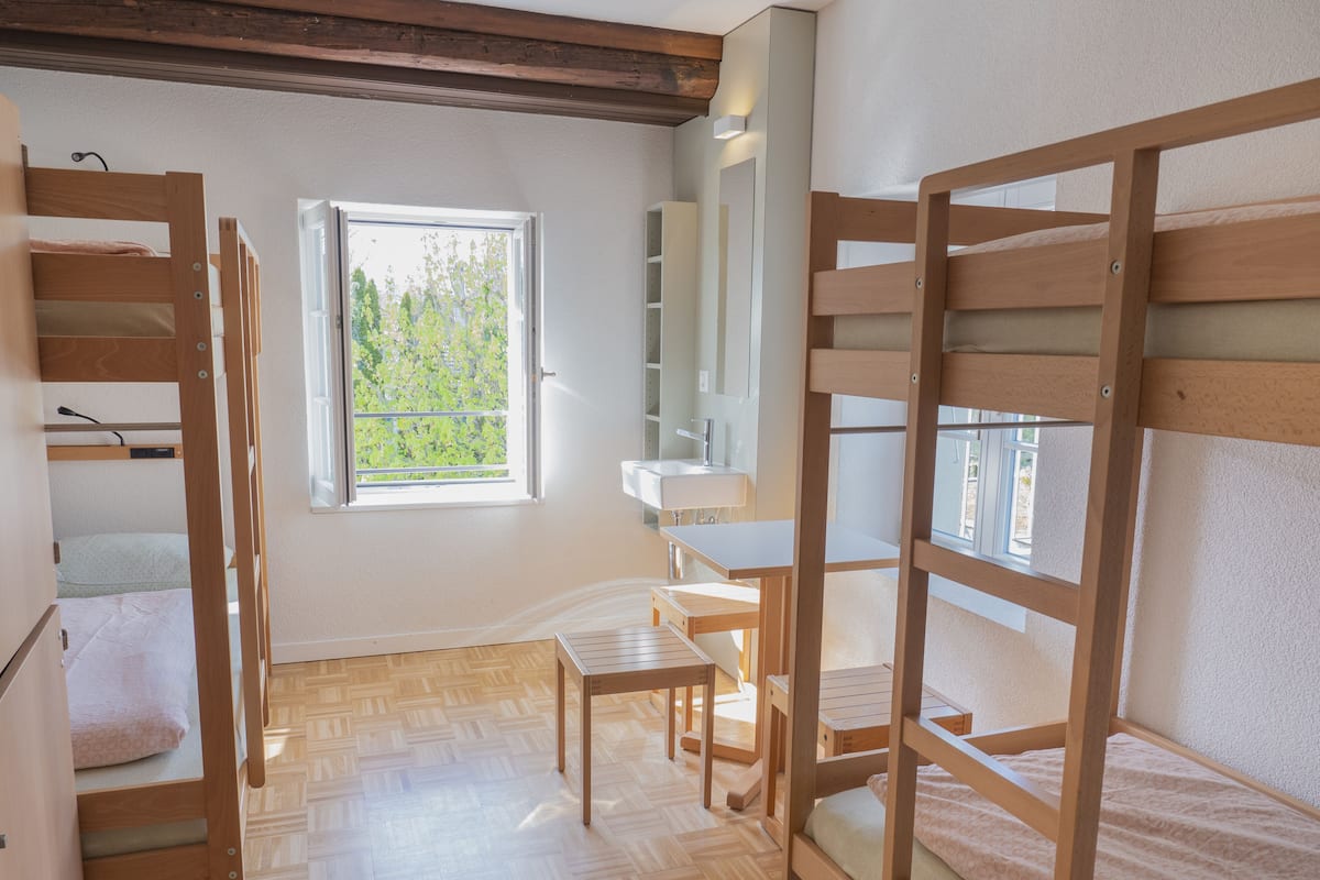 A compact room with bunk beds, a small table, a chair, a window, and a sink.
