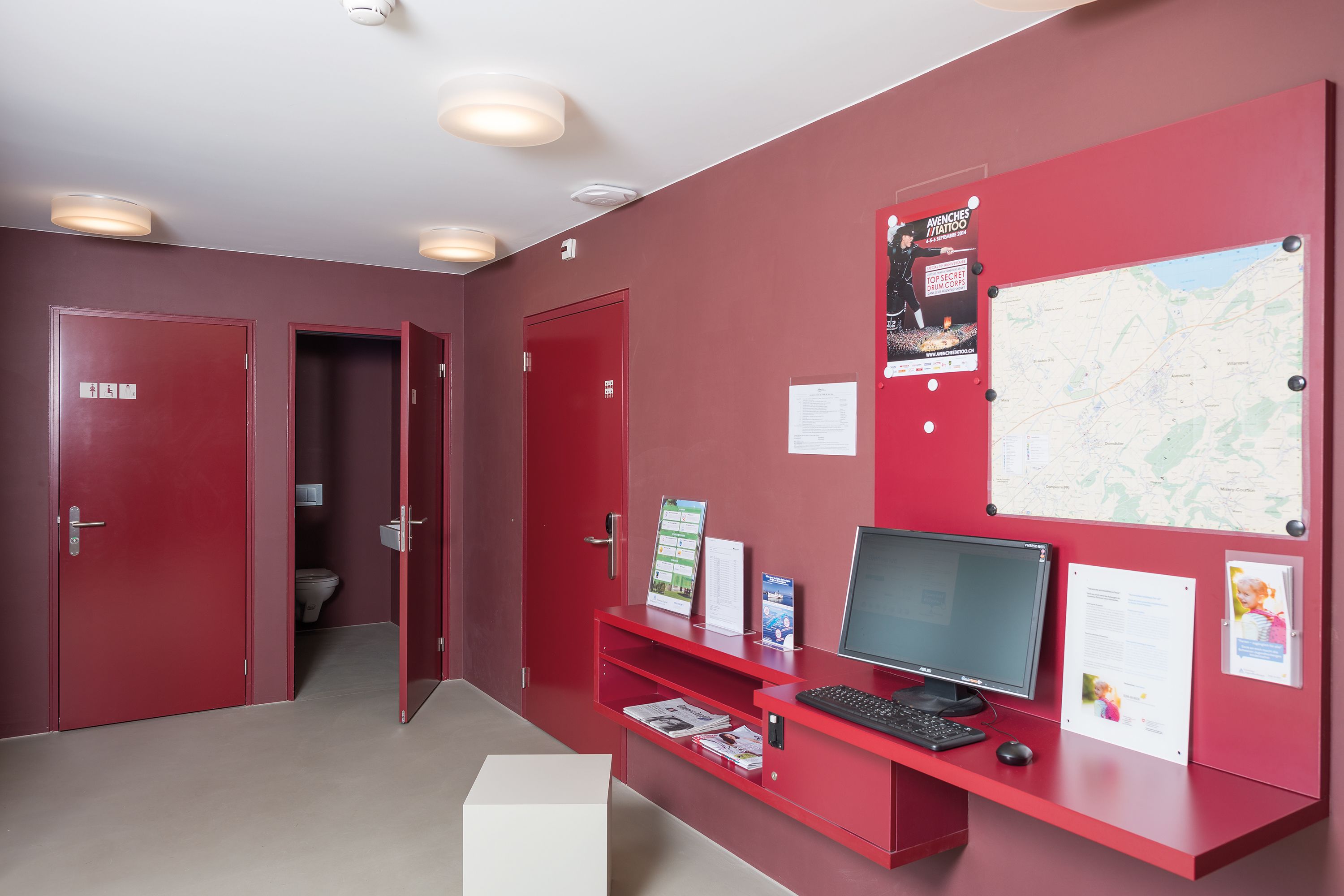 A red reception desk with a computer, a map, and informational posters.