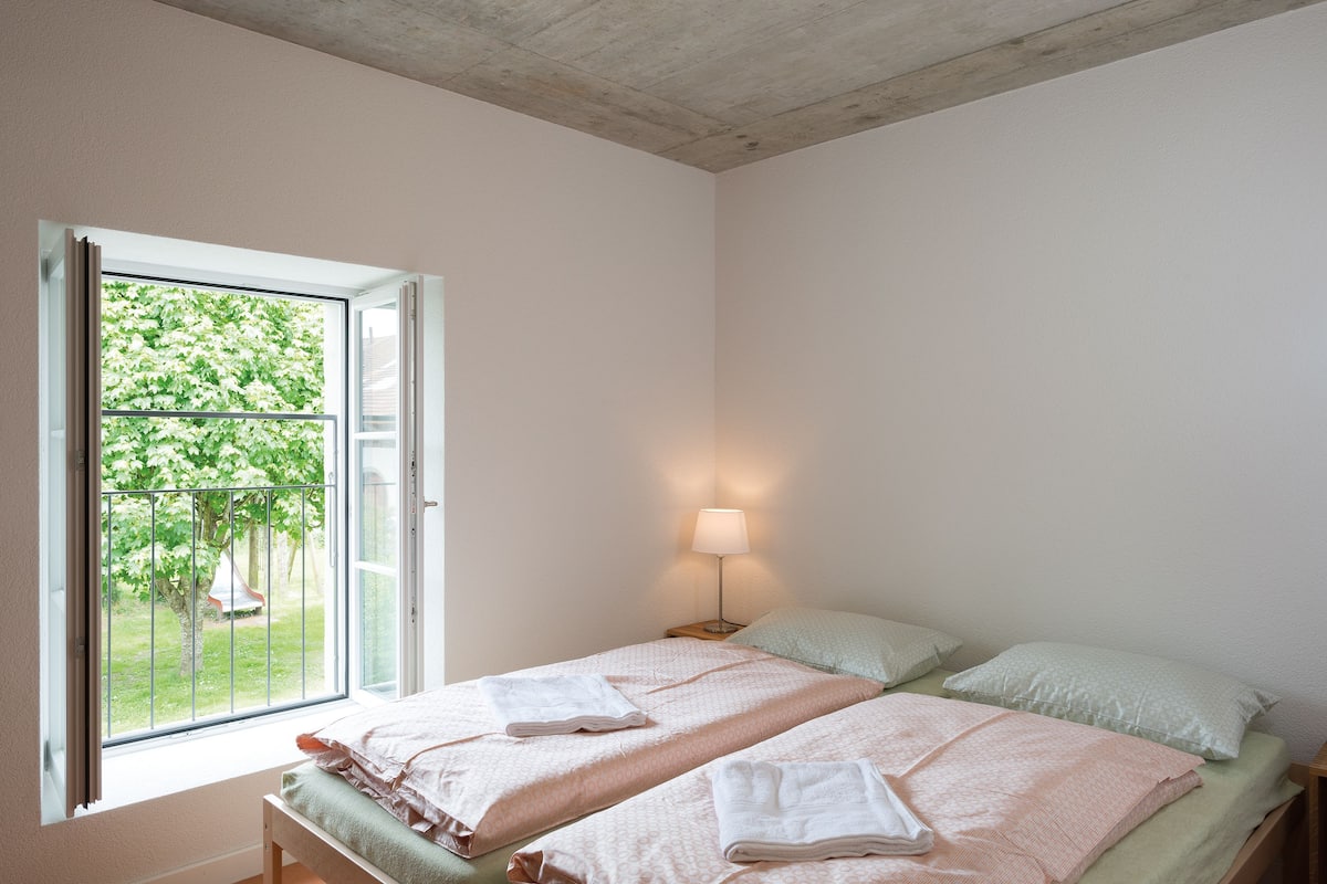 A bedroom with two beds, a window, and a nightstand with a lamp.