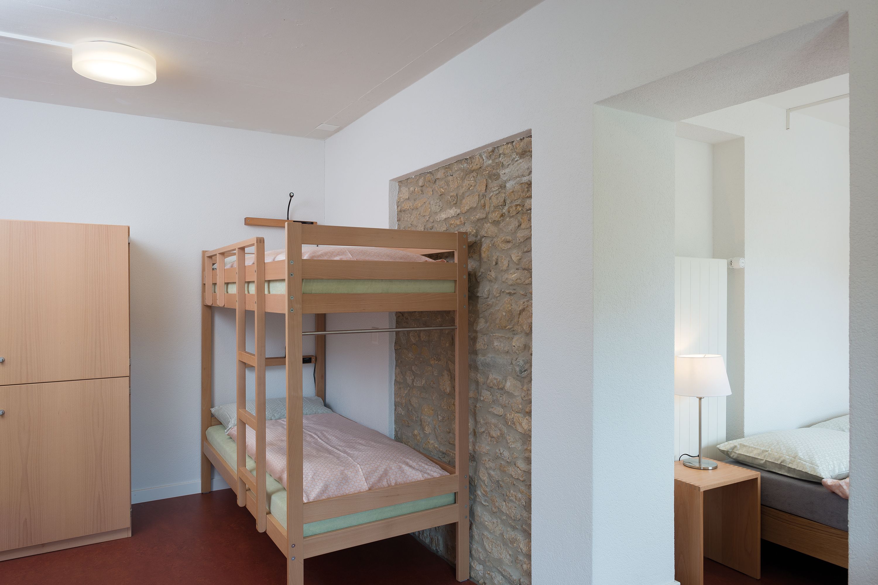 Un lit superposé avec une structure en bois, une petite table de chevet avec une lampe et une armoire.
