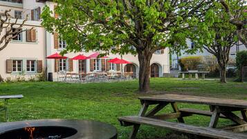 Ein Innenhof mit Feuerstelle, Picknicktisch und Sitzbereich im Freien mit roten Sonnenschirmen.