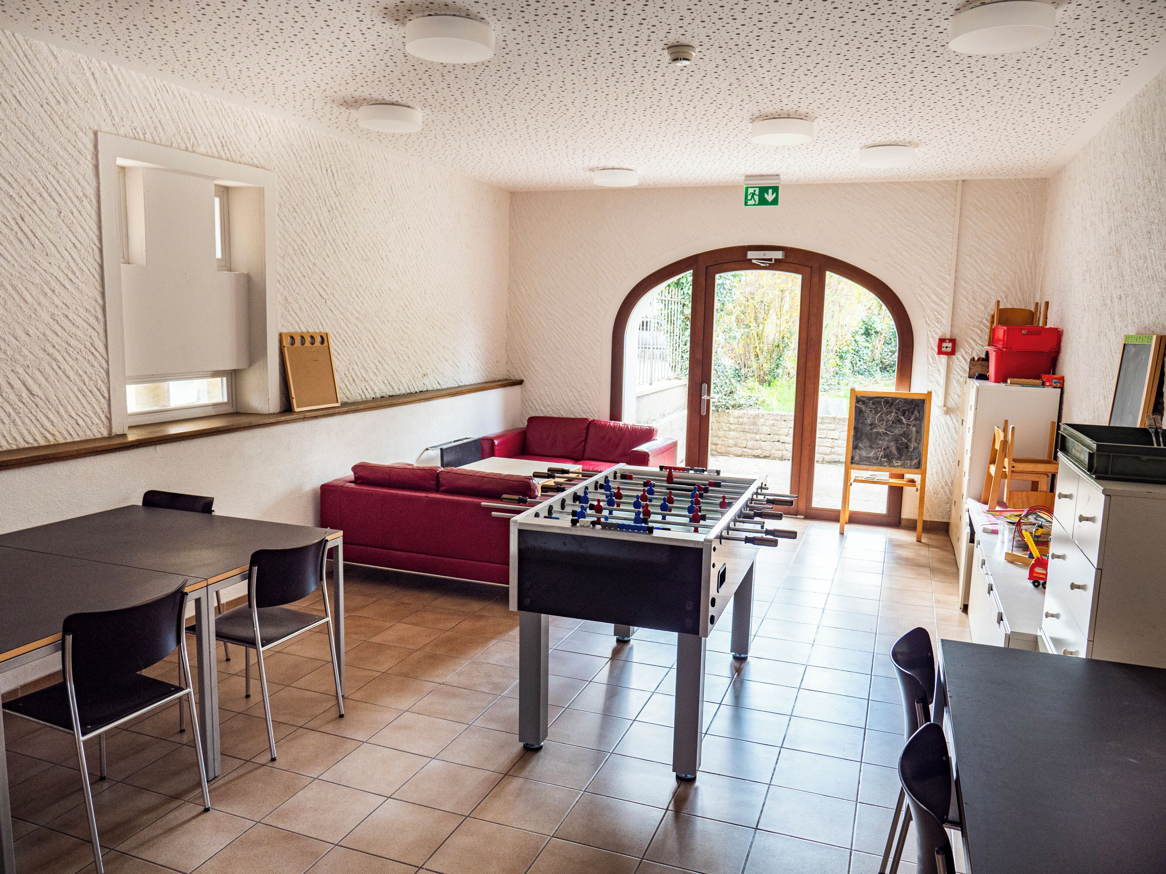 Ein Raum mit einem Tischfußballtisch, einem roten Sofa, einem Esstisch mit Stühlen und einer Kreidetafel.
