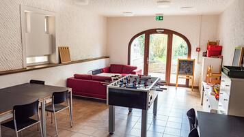 Ein Raum mit einem Tischfußballtisch, einem roten Sofa, einem Esstisch mit Stühlen und einer Kreidetafel.