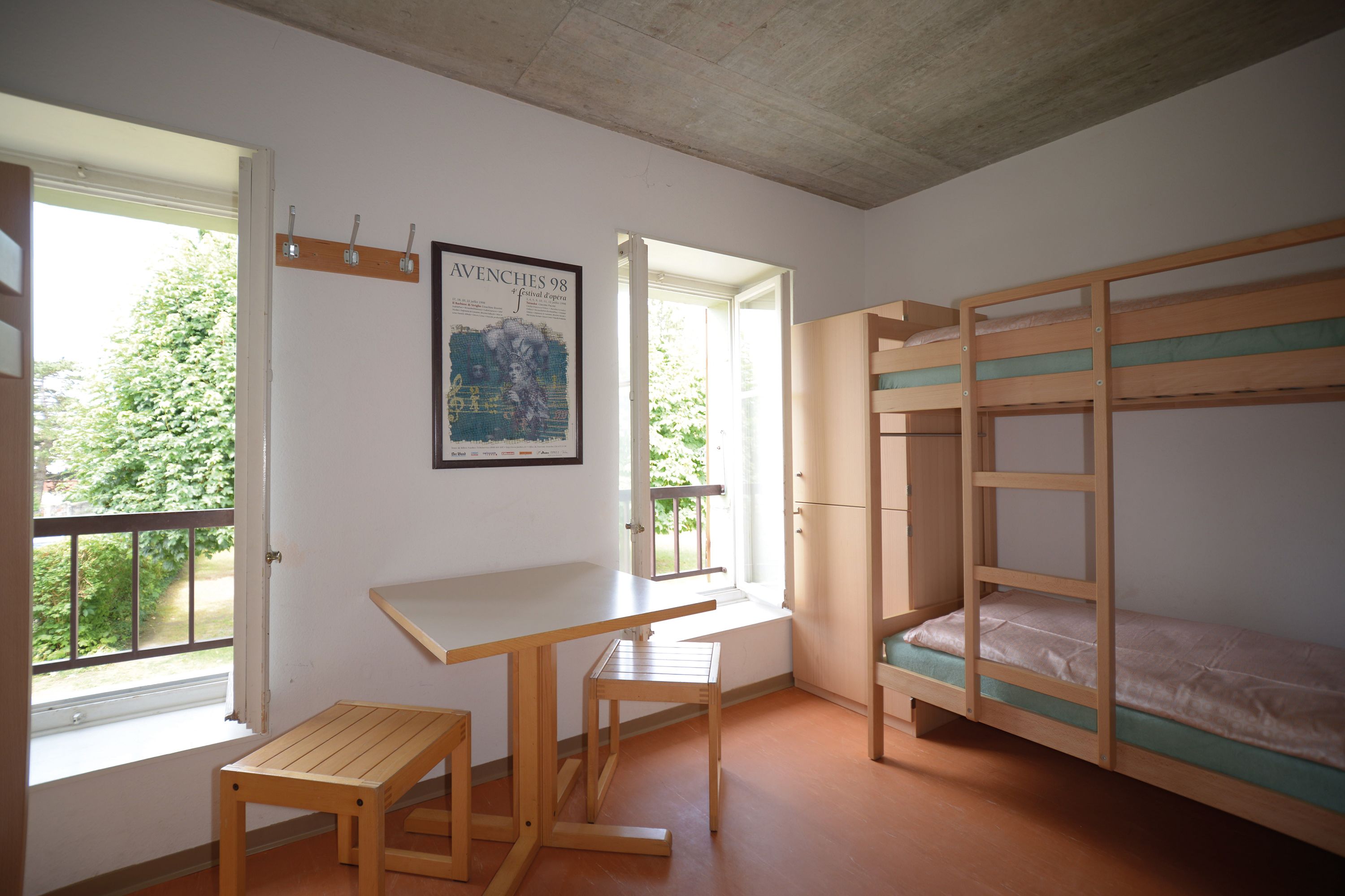 Quarto com uma cama de solteiro, uma escrivaninha e uma janela.