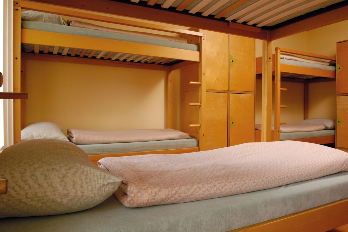 A bunk bed room with a wooden bunk bed, a single bed, and a wardrobe.
