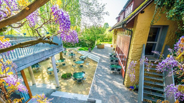 A courtyard with outdoor seating, a staircase, and a building with a yellow facade. - Youth Hostel Beinwil am See (Beinwil am See)