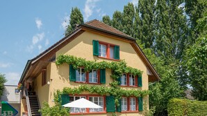 A two-story building with green shutters, a staircase, and a patio area with a table and chairs. - Youth Hostel Beinwil am See (Beinwil am See)