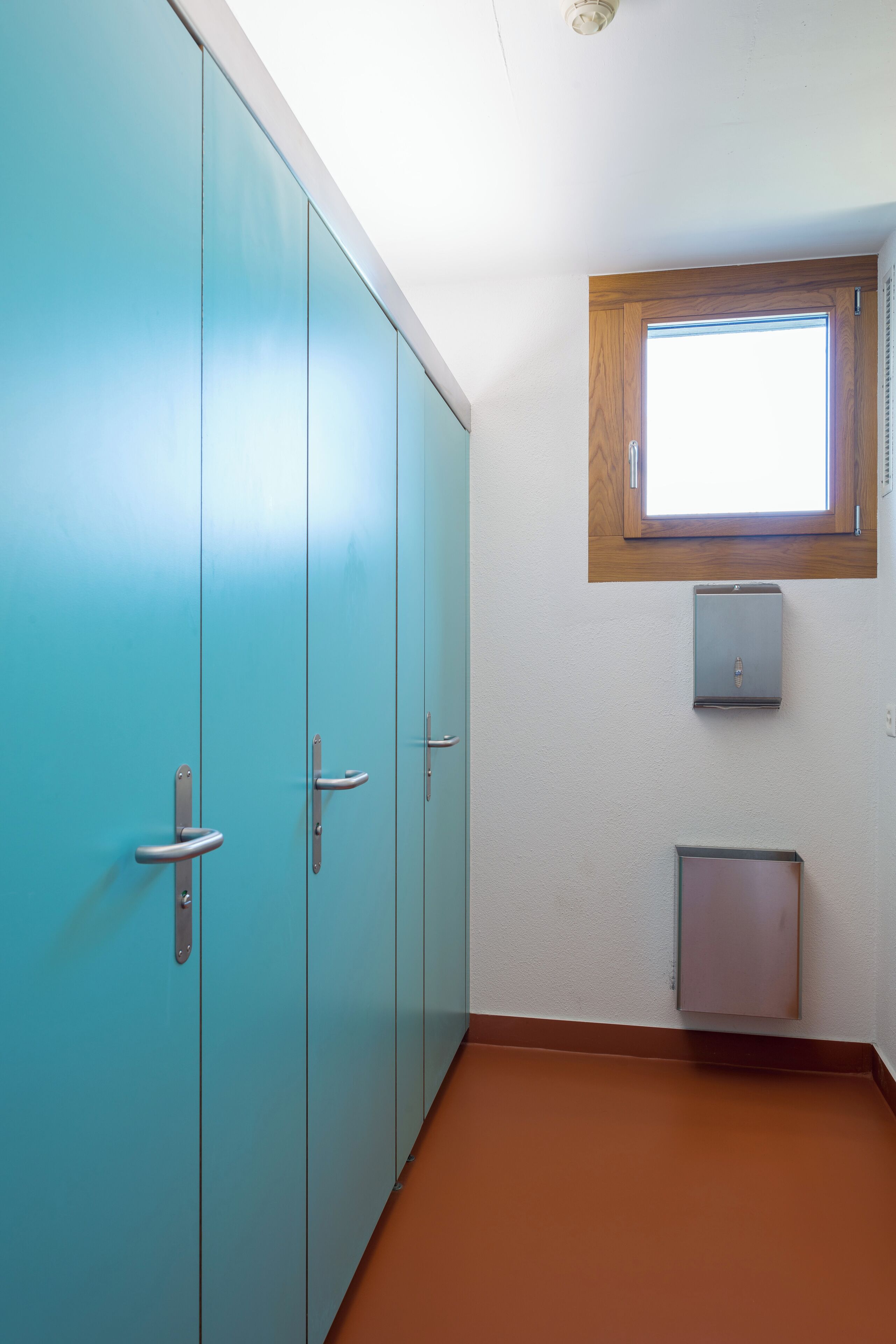 Ein Zimmer mit türkisfarbenen Schränken, einem Fenster mit Holzrahmen und einem kleinen Schrank.