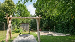 A wooden swing set in a grassy area with trees and a fenced enclosure. - Youth Hostel Beinwil am See (Beinwil am See)