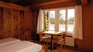 A wooden cabin room with a bed, a table, two chairs, and a window with curtains. - Youth Hostel Beinwil am See (Beinwil am See)