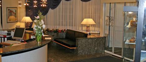 Zona de recepción de un hotel con un mostrador curvo, dos lámparas, un sofá y un jarrón decorativo.