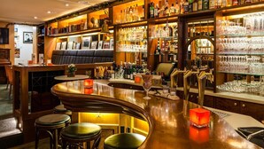 Een bar met een gebogen toonbank, stoelen en een divers aanbod aan flessen en glazen.