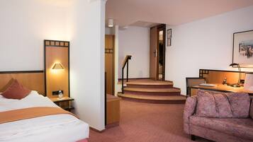 A hotel room with a bed, a sofa, a desk, a lamp, a picture on the wall, and a staircase.