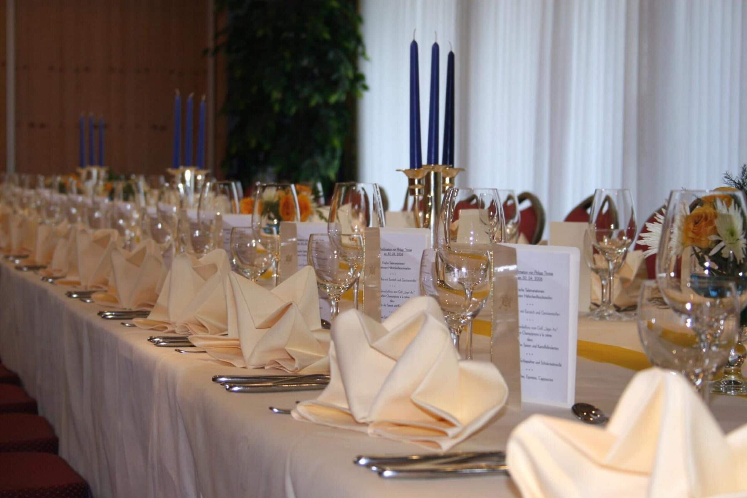 A long table set for a formal event with multiple wine glasses, folded napkins, and menus.