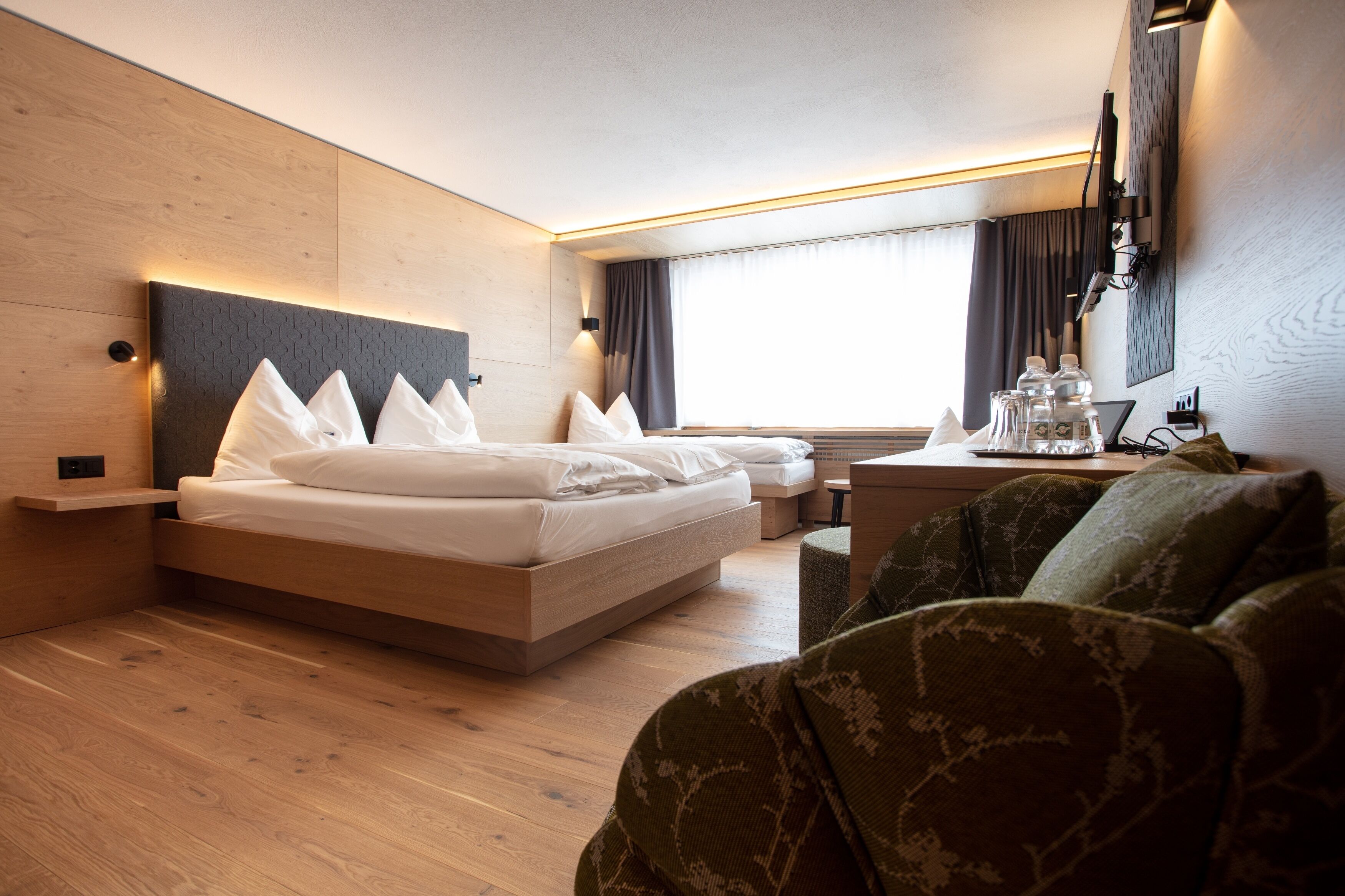 Una habitación de hotel moderna con una cama grande, mesitas de noche, un escritorio pequeño y un ventanal con cortinas.
