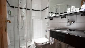 Un baño moderno con ducha envuelta en vidrio, inodoro blanco y lavamanos sobre encimera negra.