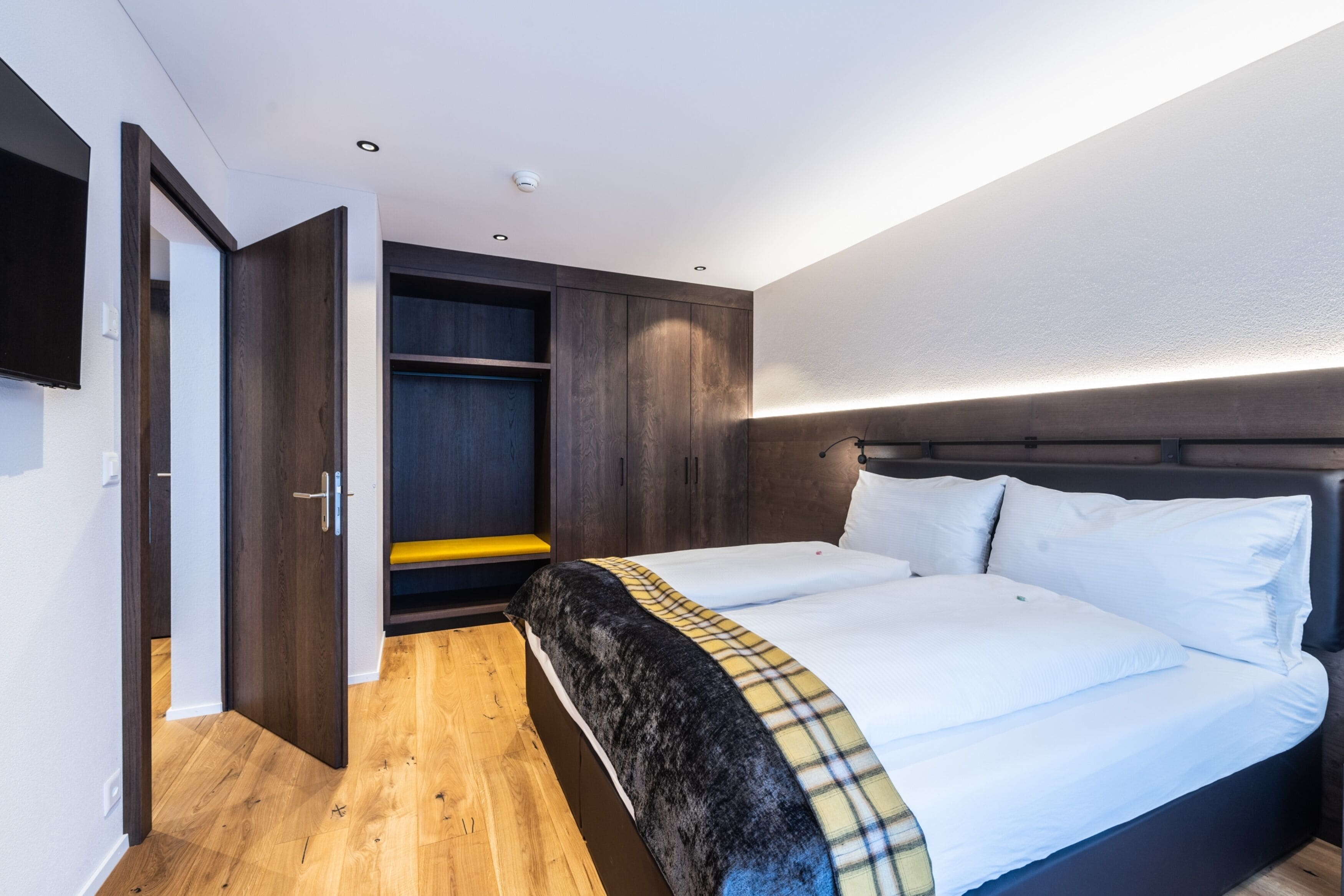 A modern bedroom with a large bed, a wardrobe, and a built-in TV.