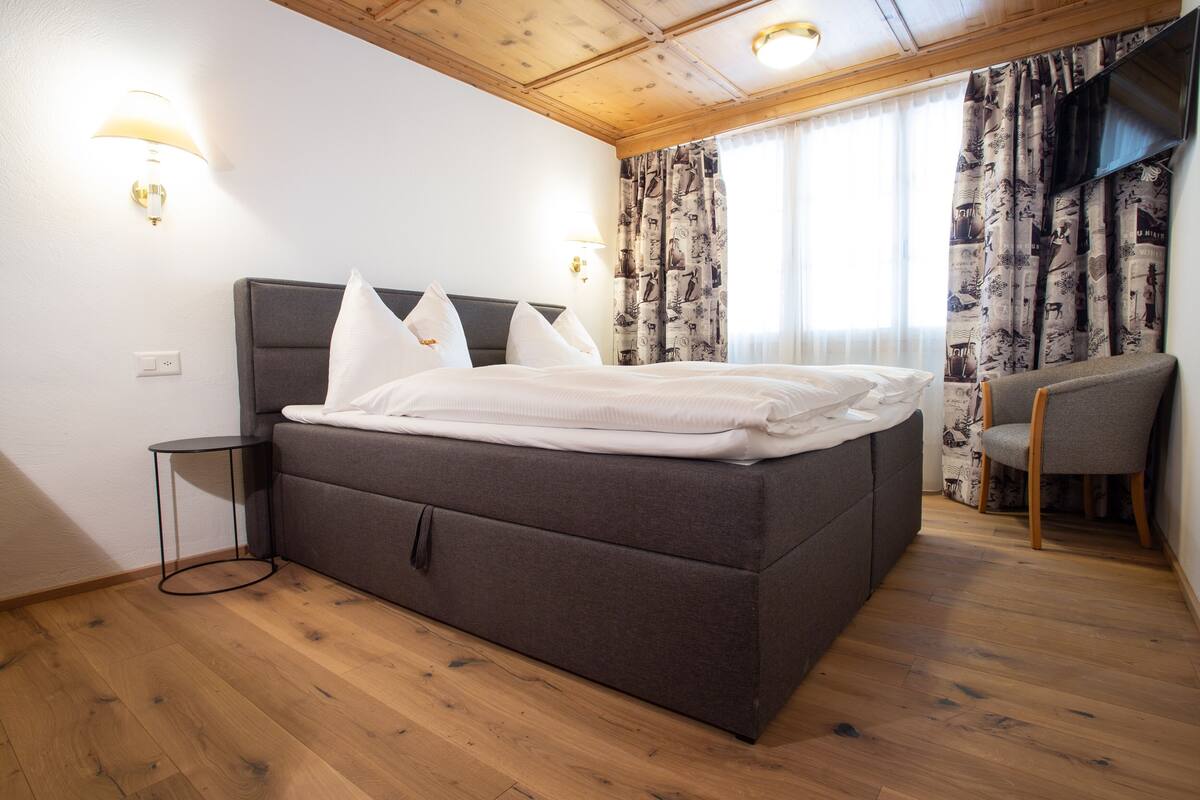 Une chambre à coucher avec un grand lit, une table de chevet, une chaise et un téléviseur fixé au mur.