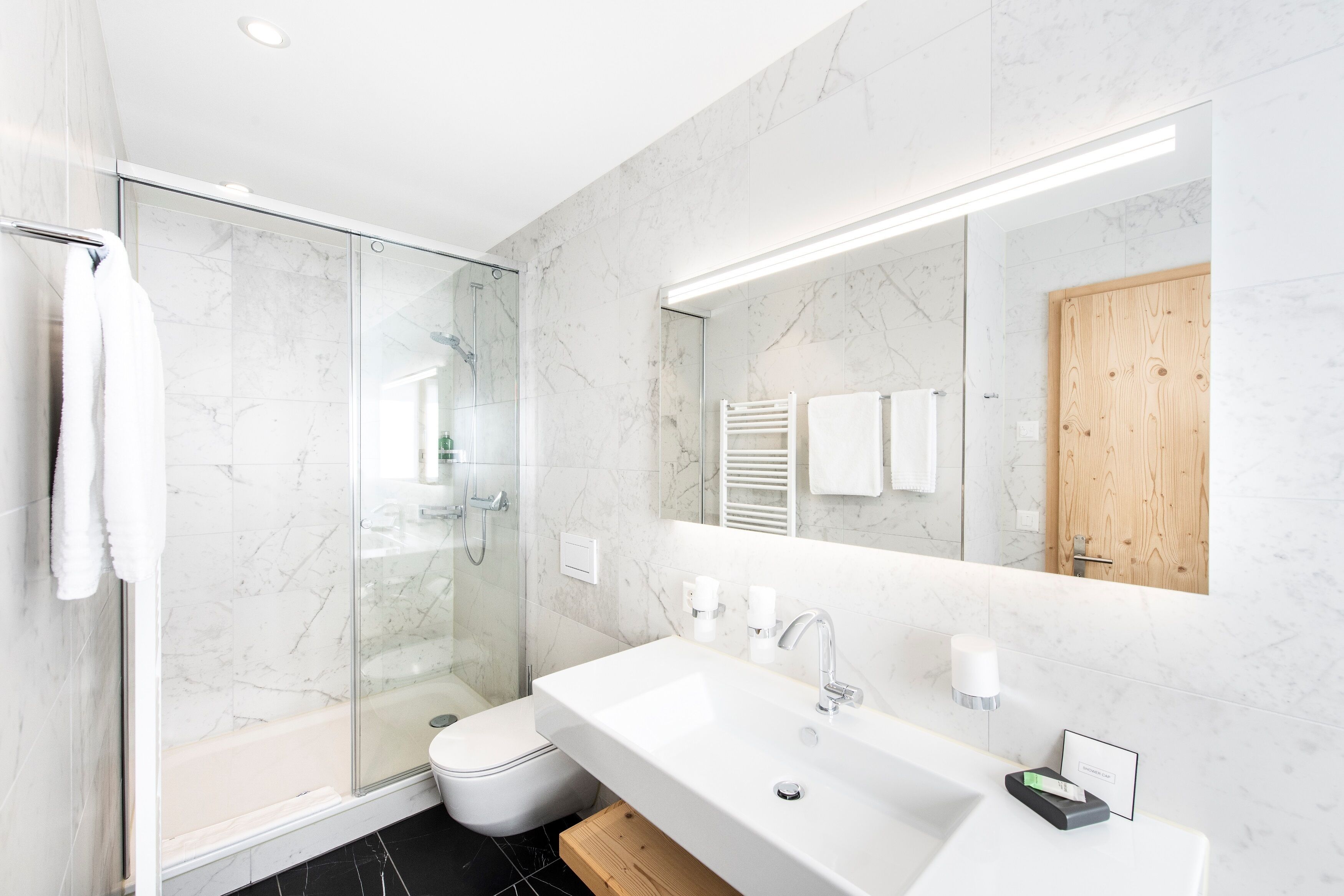Une salle de bain moderne avec une douche à l’italienne en verre, un lavabo blanc et un grand miroir.