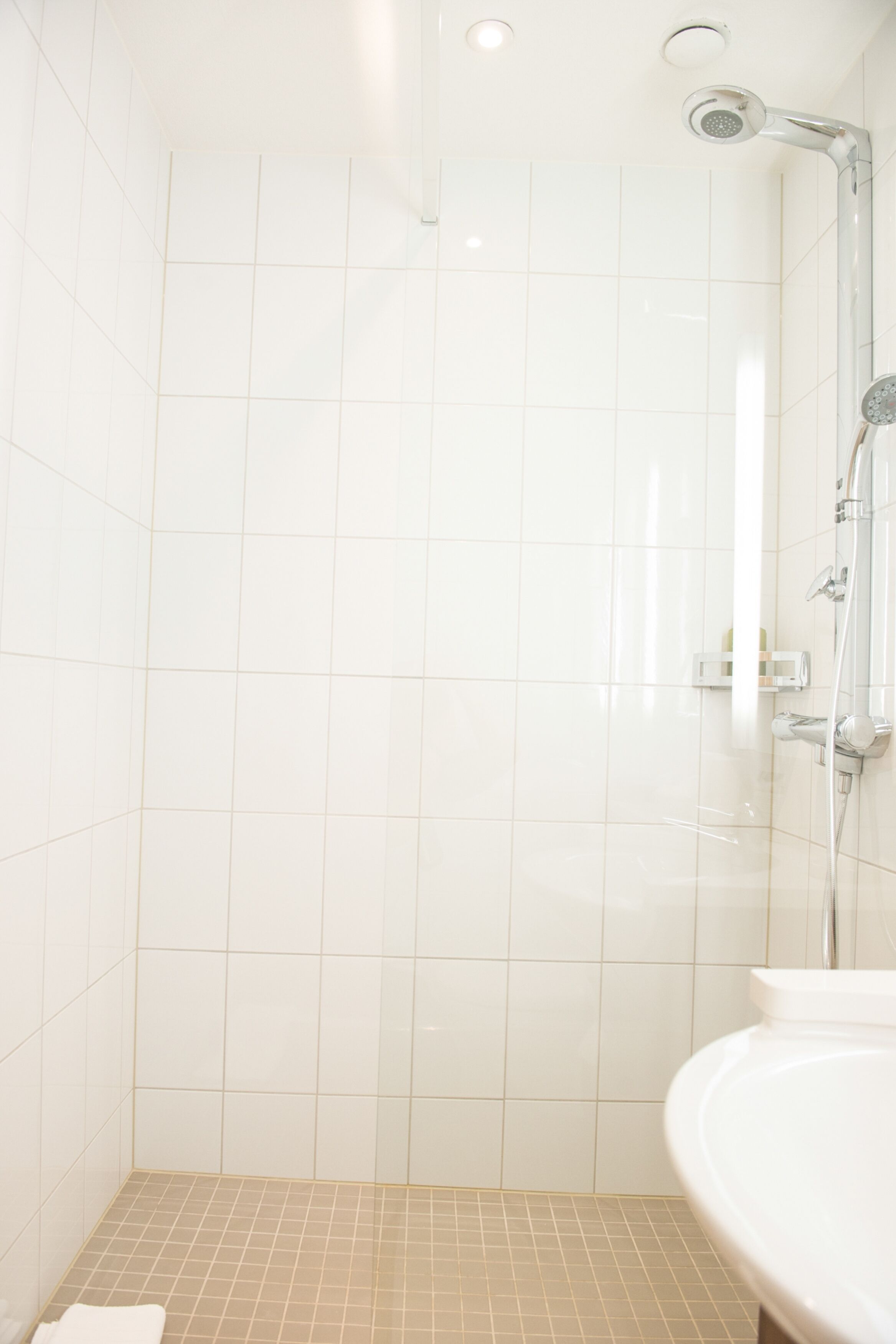 A bathroom with white tiles, a shower, and a sink.