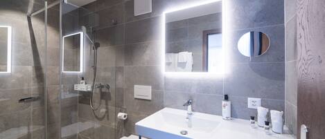 A modern bathroom with a glass-enclosed shower, a white sink with toiletries, and a large mirror.