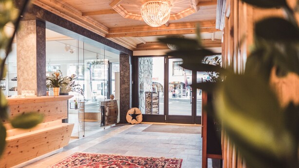 A lobby with a wooden reception desk, a large patterned rug, and a star-shaped wall decoration. - Posthotel Valbella - Berge, Spa & Wir (Vaz-Obervaz)