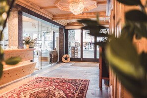 A lobby with a wooden reception desk, a large patterned rug, and a star-shaped wall decoration. - Posthotel Valbella - Berge, Spa & Wir (Vaz-Obervaz)