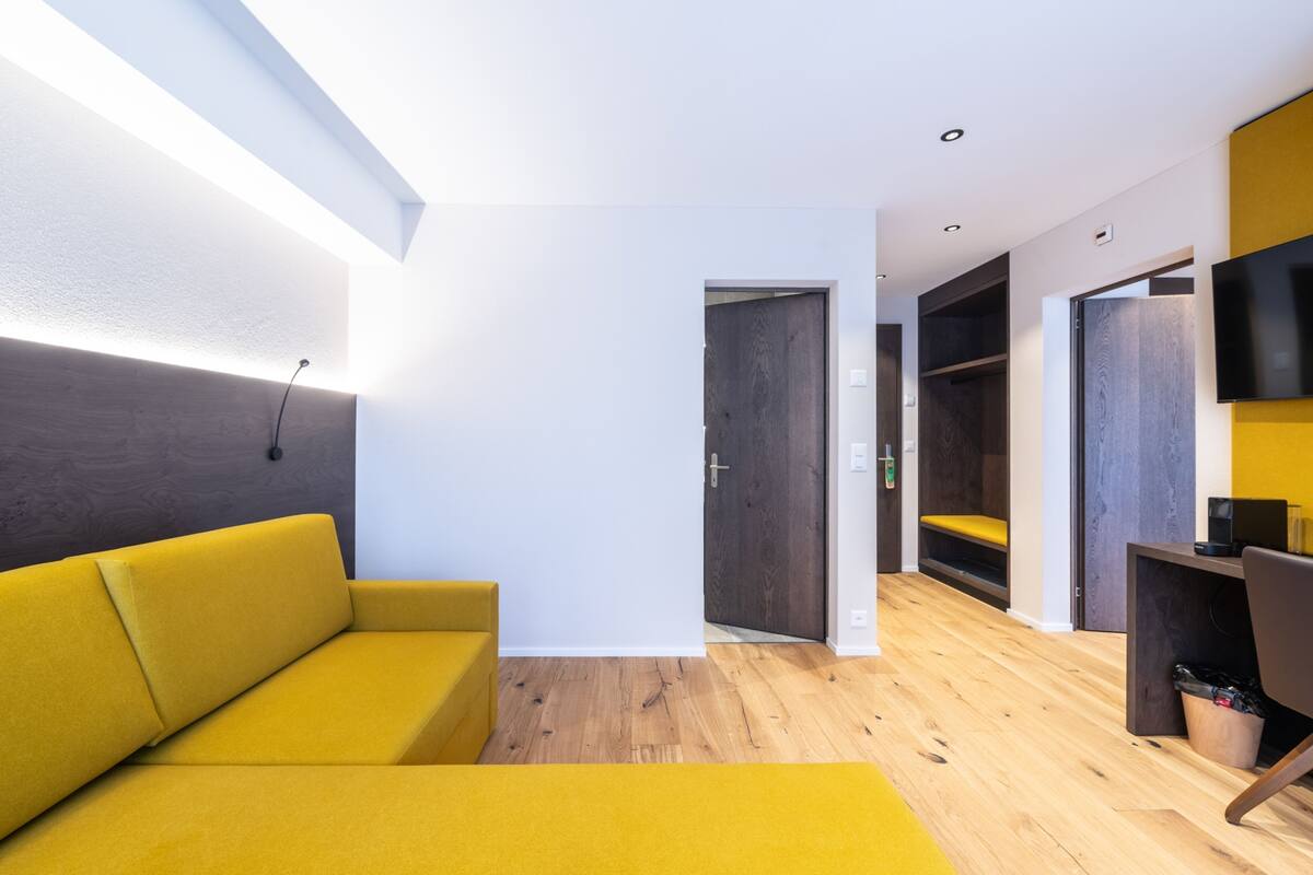 Une pièce moderne avec un canapé jaune, un plancher en bois et des étagères intégrées.
