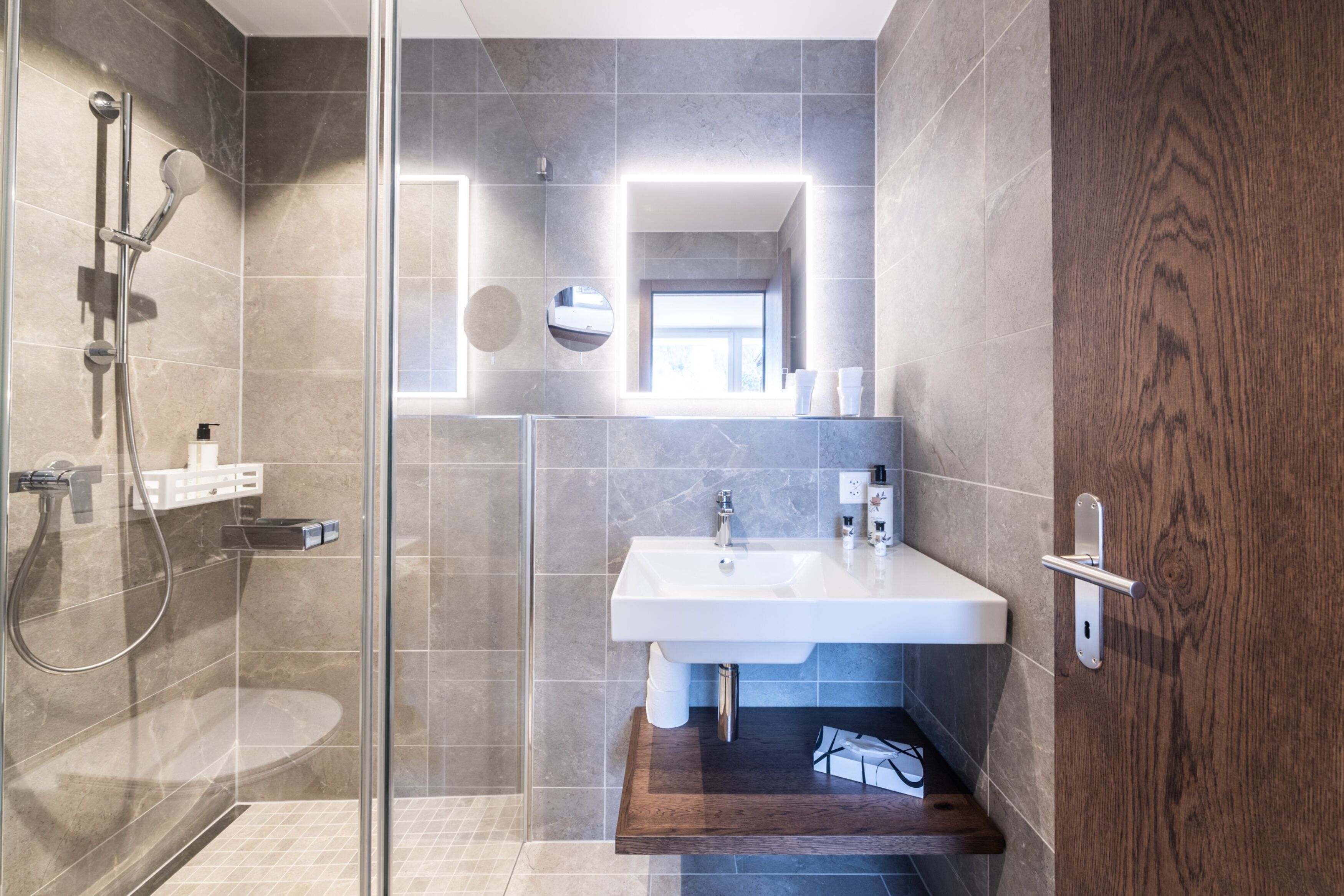 Une salle de bain moderne avec une douche à parois de verre, un lavabo blanc et un meuble-lavabo en bois.