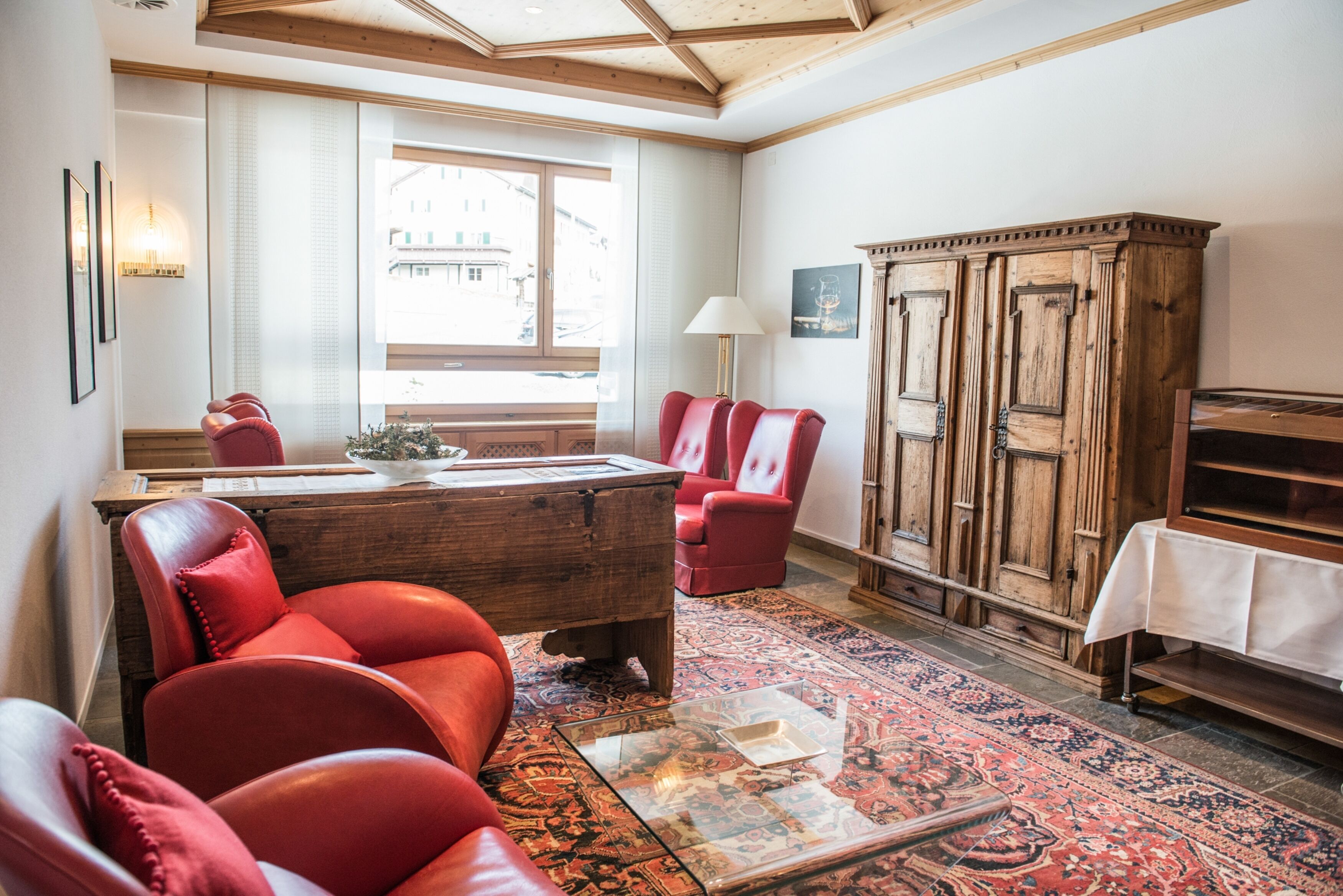 A room with a wooden coffee table, red leather chairs, a cabinet, and a patterned rug.