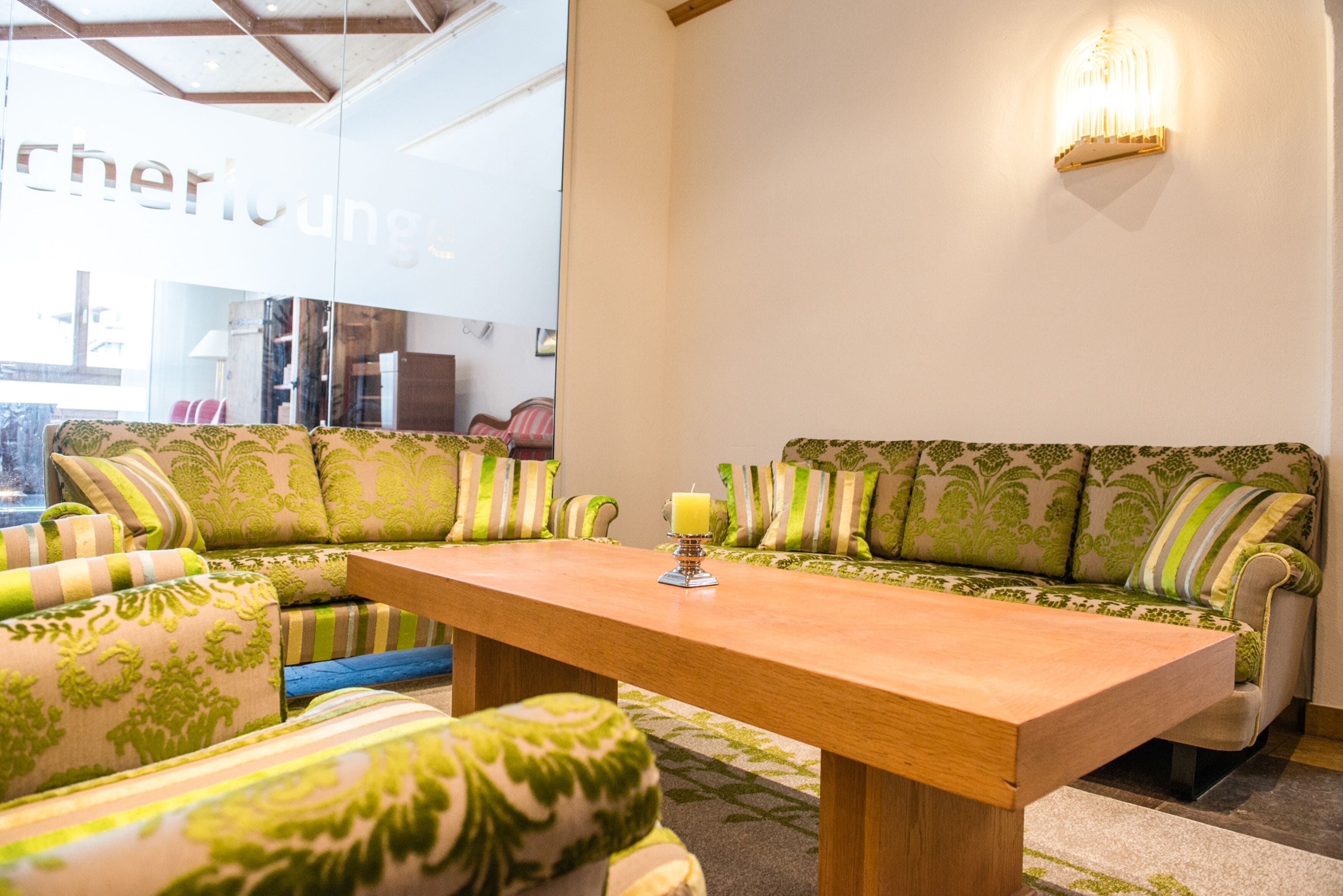 Ein modernes Wohnzimmer mit einem Holztisch, gemusterten grünen Sofas und einer Wandleuchte.