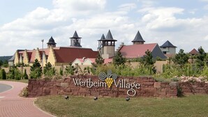 A brick pathway leading to a sign with 'Wertheim Village' and a logo. - Hotel Drei Lilien (Werbach)