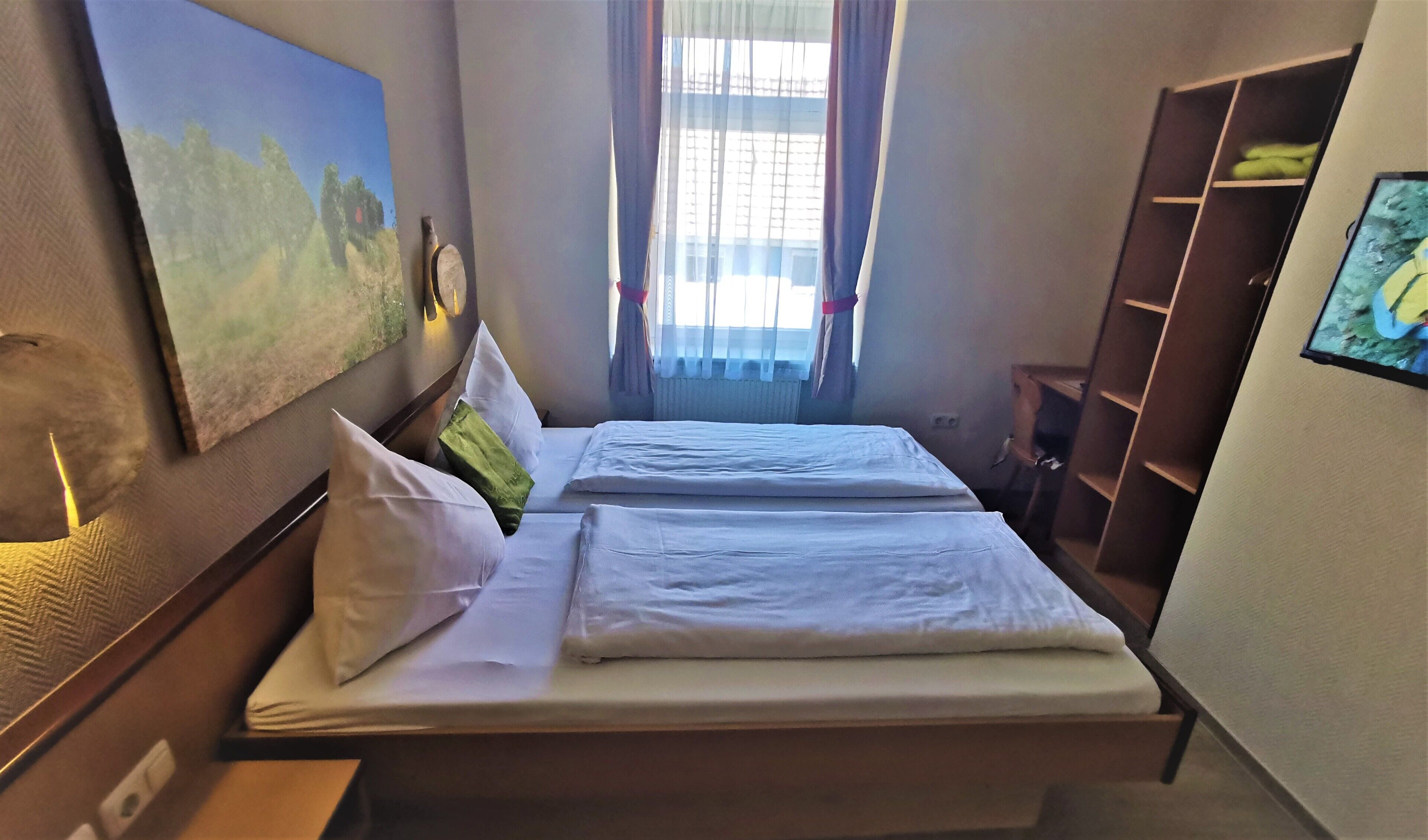 A hotel room with two beds, a painting on the wall, a window with curtains, and a wardrobe.