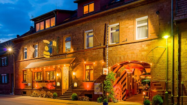 A brick building with a staircase leading to an entrance, a signboard, and a well-lit facade. - Hotel Drei Lilien (Werbach)