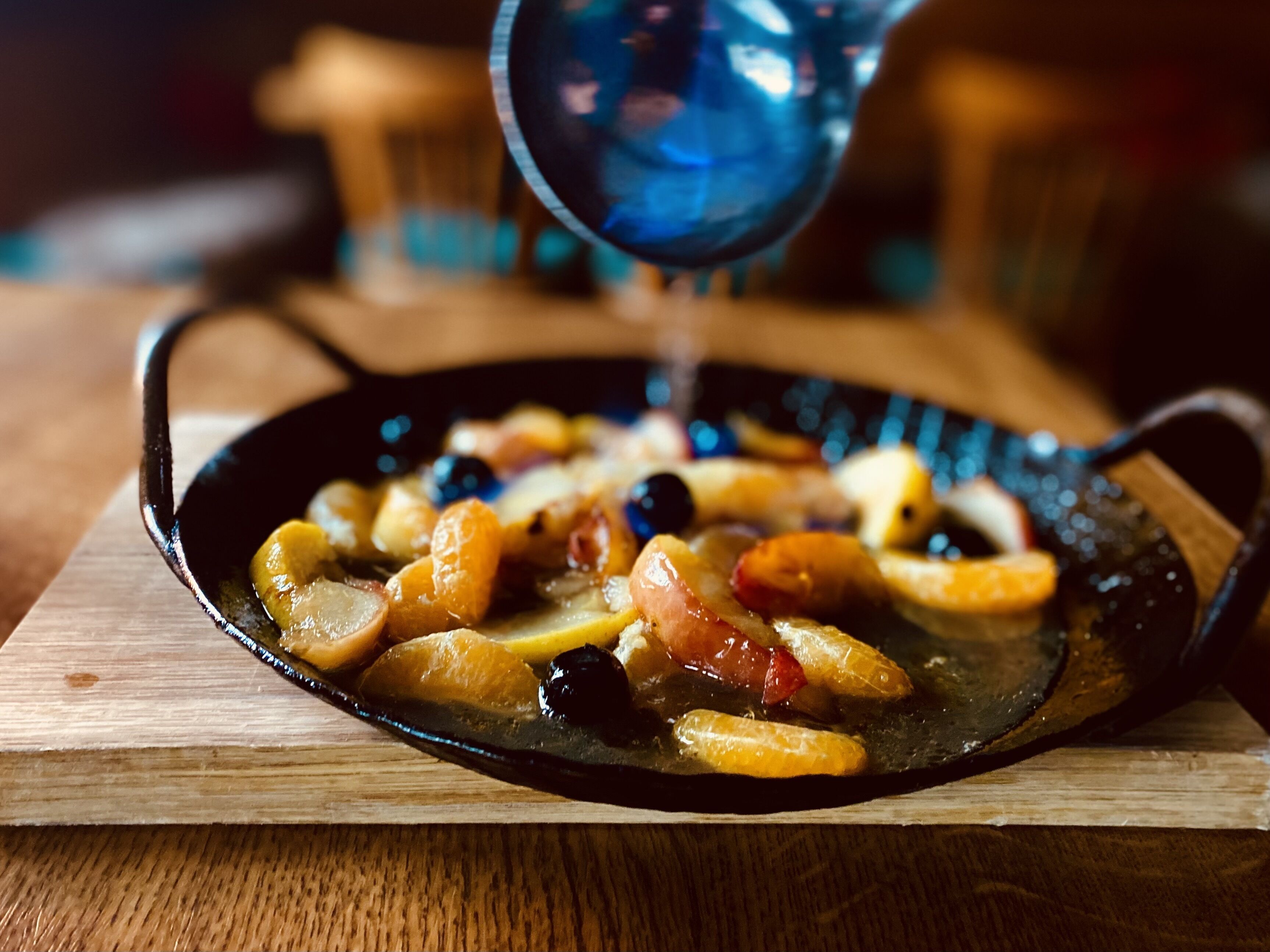 A skillet with fruits and a liquid being poured over them.