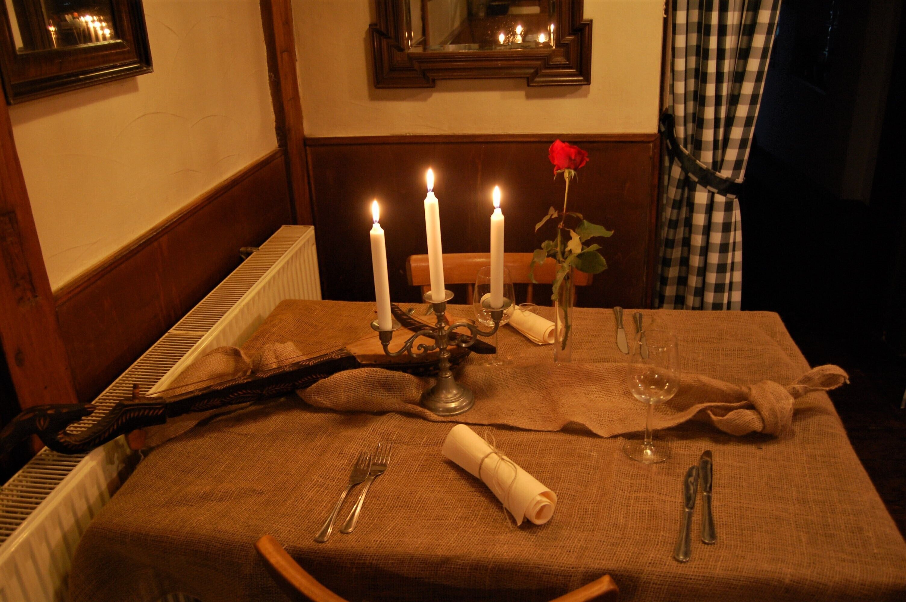 Una mesa de comedor dispuesta con velas, una rosa y cubiertos.
