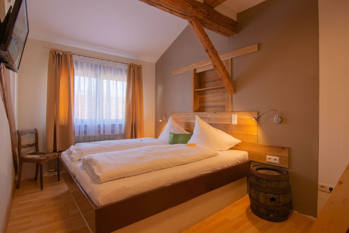 A bedroom with a wooden bed, a chair, a wooden barrel, and a window with curtains.