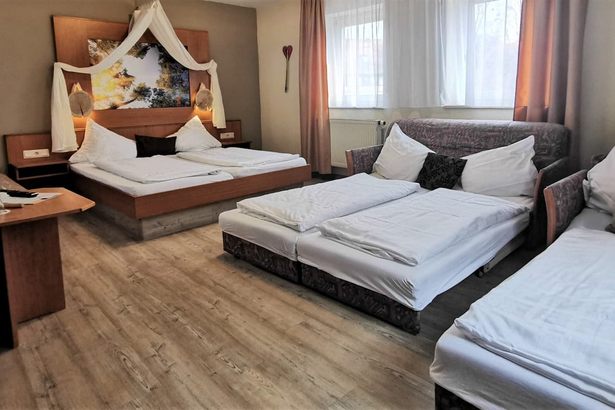 A hotel room with two single beds, a sofa bed, a desk, and a television.