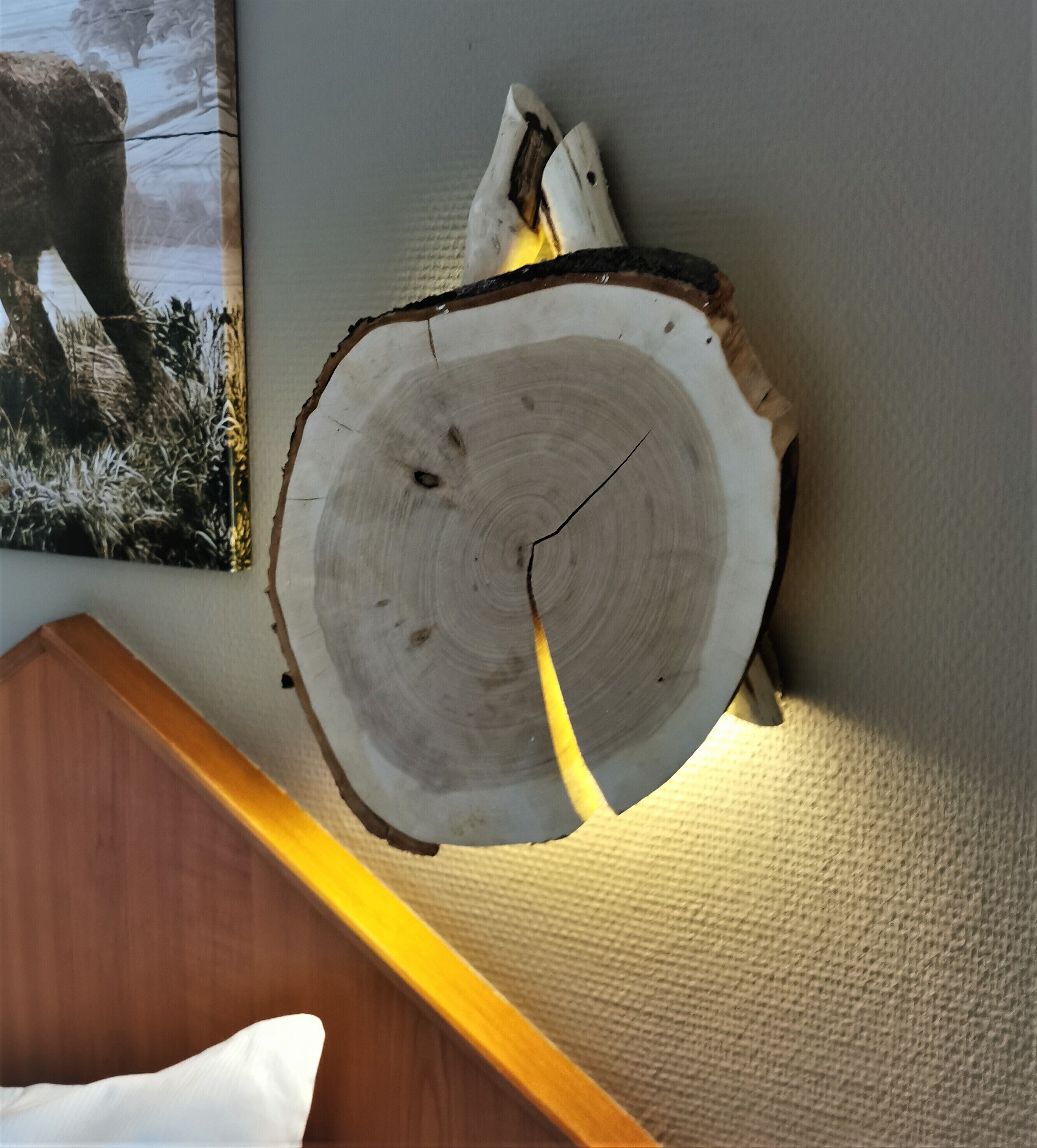 A wooden log wall clock with a visible crack, mounted on a textured wall.