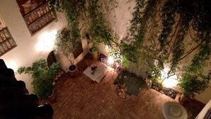 An indoor courtyard with a wooden floor, potted plants, a table with chairs, and a staircase. - Riad le Coq Fou (Marrakech)