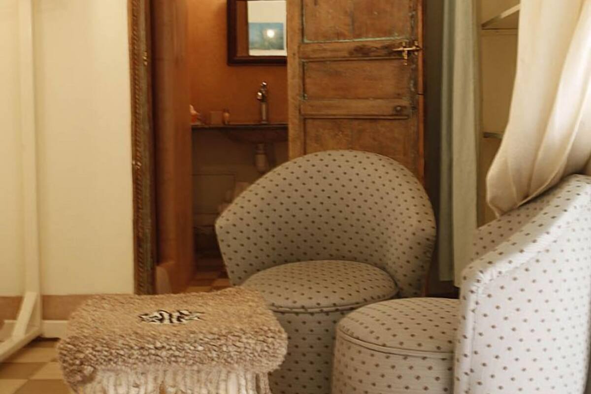 A corner room with a wooden door, a small stool, and a patterned ottoman.