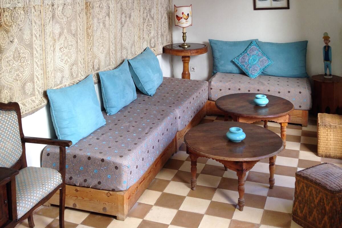 A living room with a patterned sofa, a patterned armchair, a round wooden coffee table, and two hanging wicker lamps.