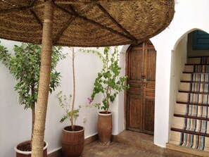 A traditional courtyard with a woven ceiling, potted plants, a wooden door, and a staircase with striped railings. - Riad le Coq Fou (Marrakech)